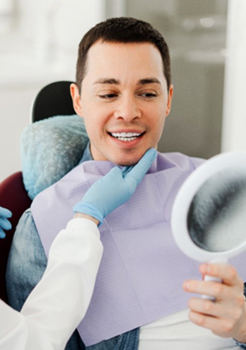 Man smiling at reflection in mirror with dentist